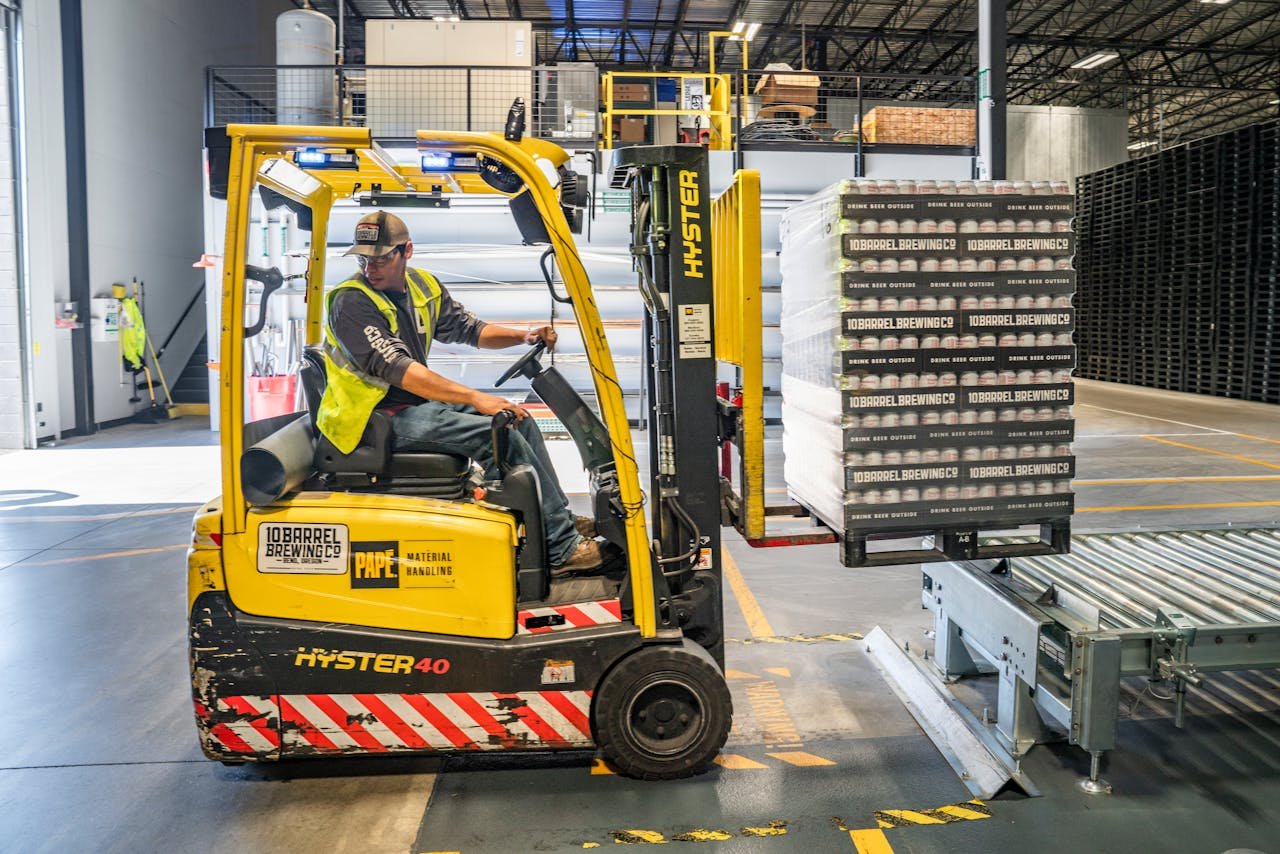Services A warehouse worker maneuvers a forklift to transport crates for brewing company storage.